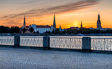 Colorful sunrise and waterfront view on historical district of Riga -capital city of Latvia, it offers for tourists many culture and resting opportunities and unique medieval and Gothic architecture - obrazy, fototapety, plakaty