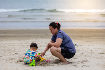 Fototapeta na wymiar An Asian Chinese baby boy with young mother on the beach playing sand. Children's games. Games on the beach