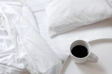 Coffee cup on table near unmade bed with messy crumpled blanket, sheet and pillow. Lifestyle morning everyday scene, neutral aesthetic background for branding identity design