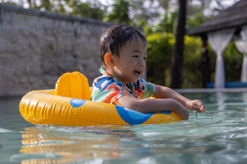 An Asian kid happy and enjoying playing water on pool with Kids' inflatable swim ring