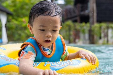 An Asian kid happy and enjoying playing water on pool with Kids' inflatable swim ring