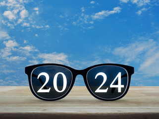 2024 white text with black eye glasses on wooden table over blue sky with white clouds, Business...