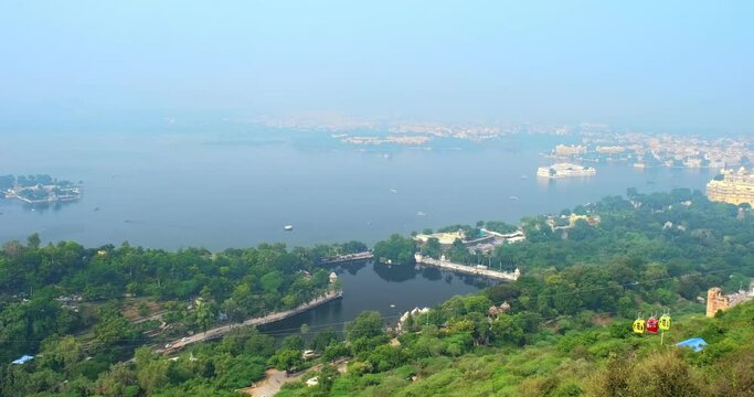 Aerial panorama of Lake Pichola with Jag Mandir Lake Garden Palace, Lake Palace (Jag Niwas) and City Palace and cable car rope way. Udaipur, Rajasthan, India. Horizontal camera pan following cable car