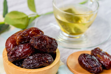 Dried dates fruit in wooden bowl with a cup of tea background.