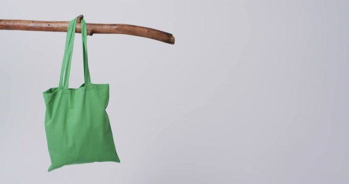Video of green canvas bags hanging from branch with copy space on white background
