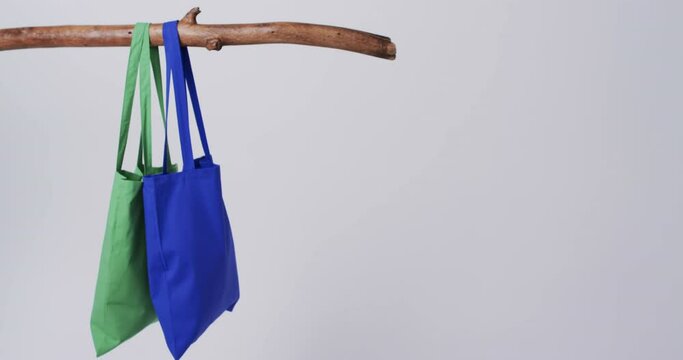 Video of green and blue canvas bags hanging from branch with copy space on white background