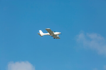 A light white plane flies across the blue sk