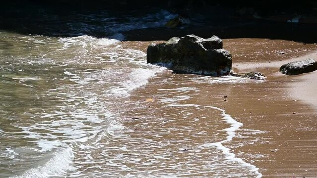 Small Waves Gently Moving onto a Beach and Against a Rock Stuck in the Sand.