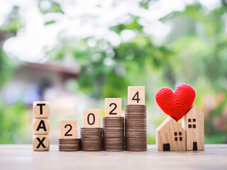 Wooden blocks with the word TAX 2024 on stack of coins and miniature house. The concept of Property...