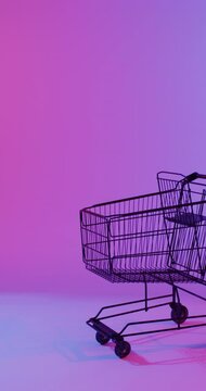 Vertical video of shopping trolley with copy space over pink neon background