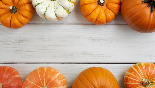Autumn top border of orange, white and striped pumpkins on a white wood background. Top view with copy space