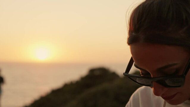 Portrait of thoughtful young woman with sunglasses looking down with sun setting in background 
