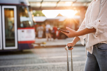 Woman using smartphone with mobile app is buying online transport ticket. Travel and public transportation in city. Tourist waiting for tram or bus at station