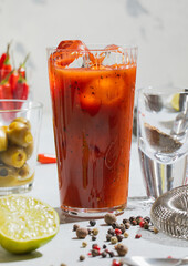 Cocktail bloody mary with pepper,lime,bar shaker and strainer on light board.