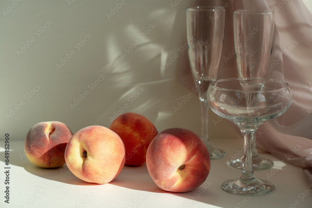 Wall mural Various wine glasses and peaches long shadow from the sun on a light beige background. Wine tasting or summer vacation concept. Beautiful fruit background.