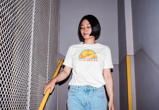 Mockup of Asian woman wearing t-shirt with customizable color and design in stairwell, camera flash