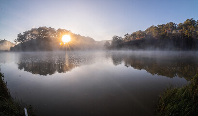 Fototapeta na wymiar Dawn in the Golden Valley is shining through the pine hills, the sun shines on the foggy surface of the lake, the beautiful scenery of Da Lat