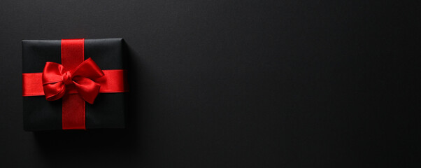Black gift box with a bow on a black background.