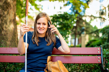 A visually impaired woman holding a white cane and having a call outside