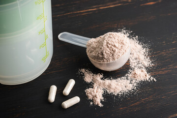 Scoop of chocolate whey protein isolate, white capsules of amino acids and creatine, bodybuilding...