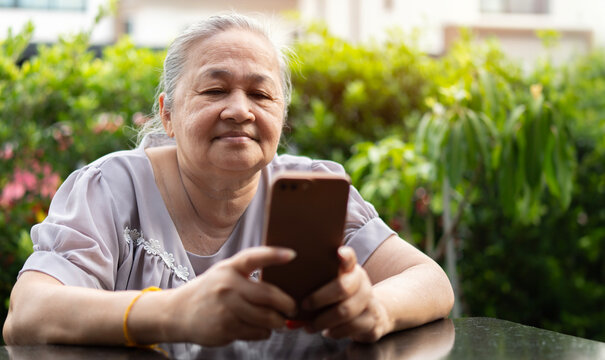 Photo of Asian old woman use smartphone and looking or texting on social media with nature background.