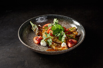 Horizontal side view of roasted eggplant paired with tomatoes, cilantro, and cheese, beautifully plated on a stone dish against a black marble setting