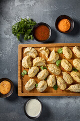 A top view horizontal shot emphasizing the variety of sauces accompanying the assortment of manti and eastern dumplings, presented on a rustic wooden board, set against a gray background