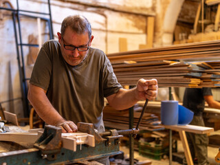 Veteran carpenter clamping a piece of wood with a bench vise in a carpentry workshop - Traditional woodworking concept.