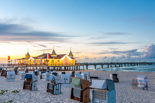 Germany, Mecklenburg-Vorpommern, Ahlbeck, Hooded beach chairs at sunset with pier and bathhouse in background