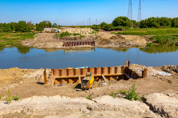 Bridge foundation made of metal piles on river coast, compressor placed at building site