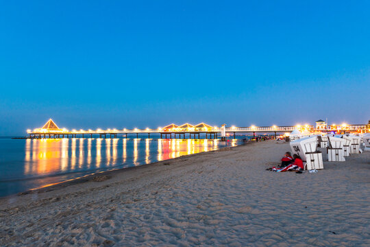 Germany, Mecklenburg-Vorpommern, Ahlbeck, Hooded beach chairs and illuminated pier at dusk