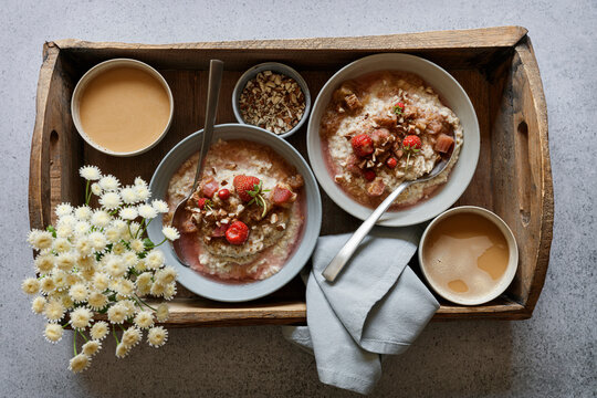 Studio shot of wooden tray with bowls of vegan porridge, wildflowers and rhubarb compote