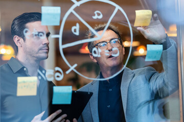 Businessman having discussion with colleague over adhesive notes and diagram on glass