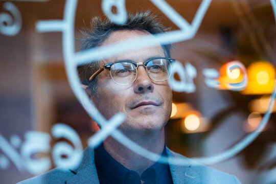 Smiling mature businessman planning strategy seen through glass in office