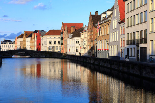 Belgium, West Flanders, Bruges, Row of riverside townhouses with arch bridge in background
