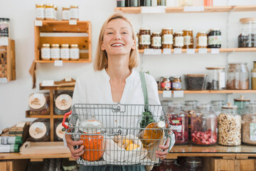 Happy woman holding basket of groceries in store