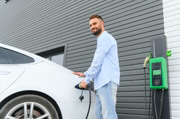 Fototapeta na wymiar Stylish man inserts plug into the electric car charging socket