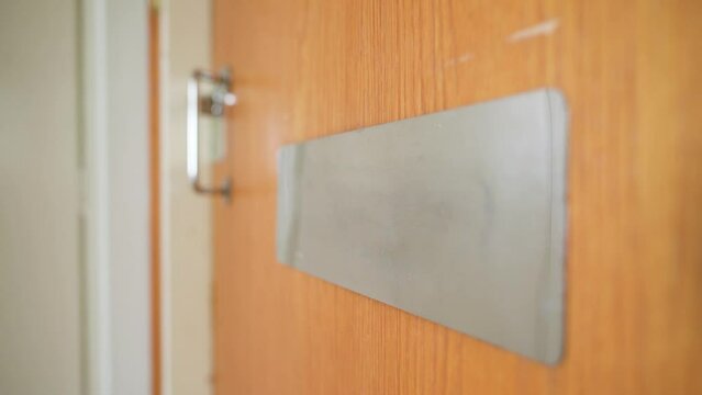 White envelope being dropped through a mail slot in the door. Wide angle close up