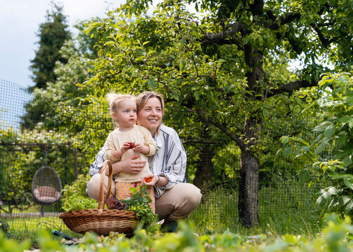 Happy mother and daughter with basket of fresh vegetables in garden
