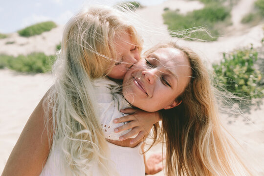 Loving daughter hugging and kissing mother on cheek at beach