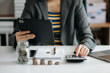 businesswoman holding coins putting in glass with using smartphone and calculator to calculate concept saving money for finance accounting in office
