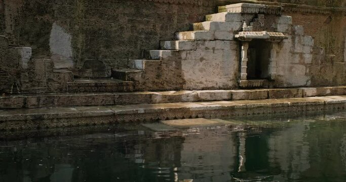 Water storage inside Toorji Ka Jhalra Baoli stepwell, one of water sources in Jodhpur, Rajasthan, India. Sunny day, water ripples reflect walls of the pool. Camera horizontal pan