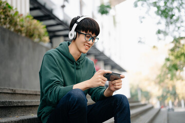 Obraz premium Young Asian man holds a cell phone in his hands typing messages or reading newsfeed.using modern gadget for entertainment playing different games online