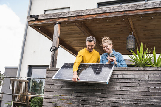 Couple installing solar panel on wooden balcony