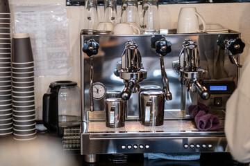 The barista prepares fresh coffee in the coffee machine in the morning in the cafe. There are coffee cups on the table for customers. Coffee machine close-up