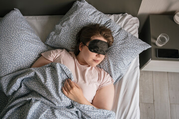 Woman wearing eye mask sleeping on bed at home