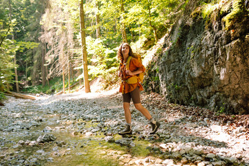 Obraz premium A traveler walks along a forest hiking trail in the mountains against the backdrop of mountain nature on a sunny day. Hiking, active lifestyle. Outdoor recreation concept.