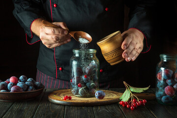 Adding sugar to a jar of plums by the chef hands. Preparing a sweet drink from fresh plums and sugar on the kitchen table. The concept of the process of preserving berries in a jar