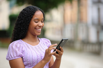 Happy black woman using smartphone in the street