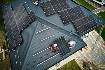 Engineers building photovoltaic solar module station on roof of house. Men electricians in helmets...